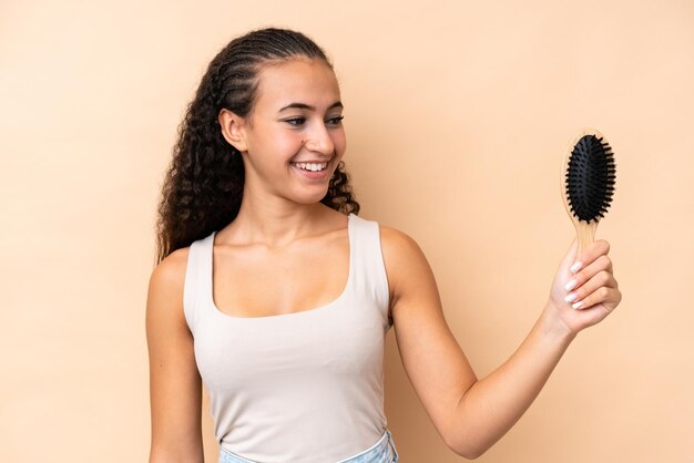 Foto jovem mulher hispânica com pente de cabelo isolado em fundo bege com expressão feliz