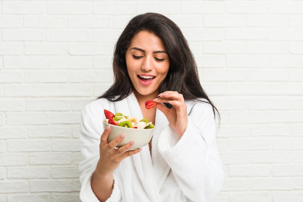 Jovem mulher hispânica, comendo uma tigela de frutas na cama