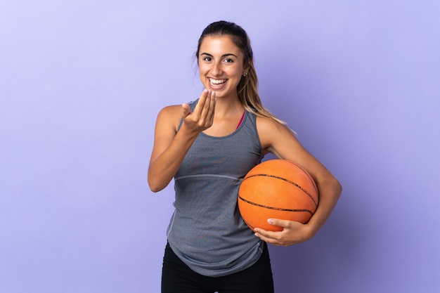 Jovem mulher hispânica em uma parede roxa isolada jogando basquete e fazendo gesto de aproximar-se