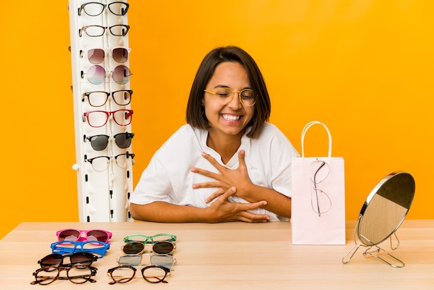 Jovem mulher hispânica experimentando óculos isolados, rindo e se divertindo.