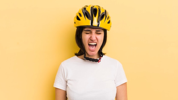 Jovem mulher hispânica gritando agressivamente olhando o conceito de capacete de bicicleta muito irritado