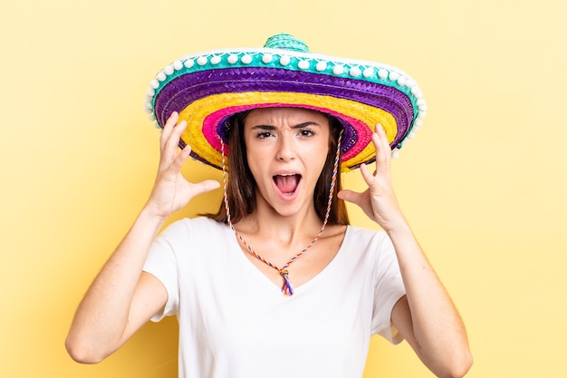 Jovem mulher hispânica gritando com as mãos no ar. conceito de chapéu mexicano