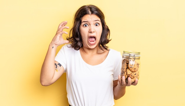 Jovem mulher hispânica gritando com as mãos para cima no conceito de garrafa de biscoitos de ar