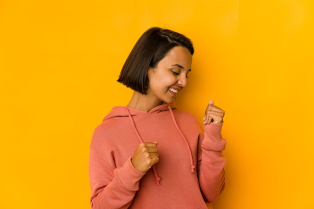 Jovem mulher hispânica isolada em amarelo, dançando e se divertindo.