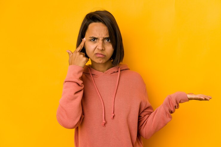 Foto jovem mulher hispânica isolada em amarelo segurando e mostrando um produto por lado.