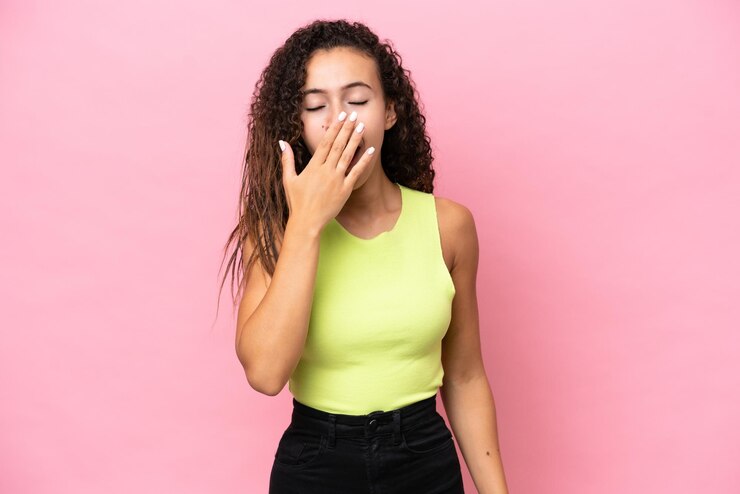 Foto jovem mulher hispânica isolada em fundo rosa bocejando e cobrindo a boca aberta com a mão