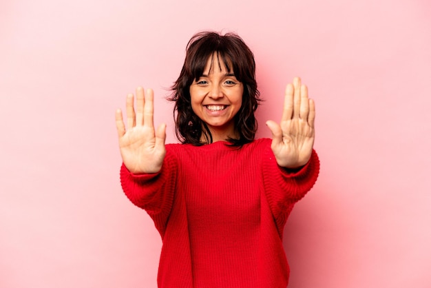 Jovem mulher hispânica isolada em fundo rosa, mostrando o número dez com as mãos