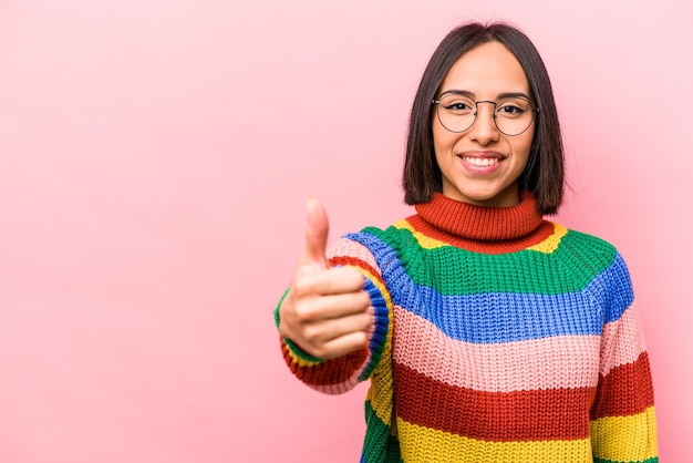 Jovem mulher hispânica isolada no fundo rosa sorrindo e levantando o polegar