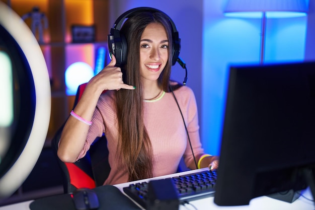 Jovem mulher hispânica jogando videogame sorrindo fazendo gesto de telefone com a mão e os dedos como falar ao telefone. comunicar conceitos.