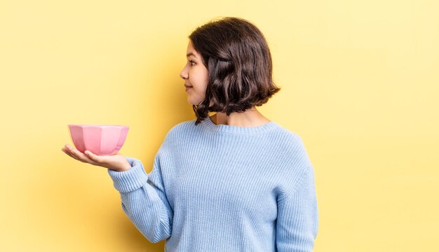 Jovem mulher hispânica na vista de perfil, pensando, imaginando ou sonhando acordada. conceito de tigela vazia