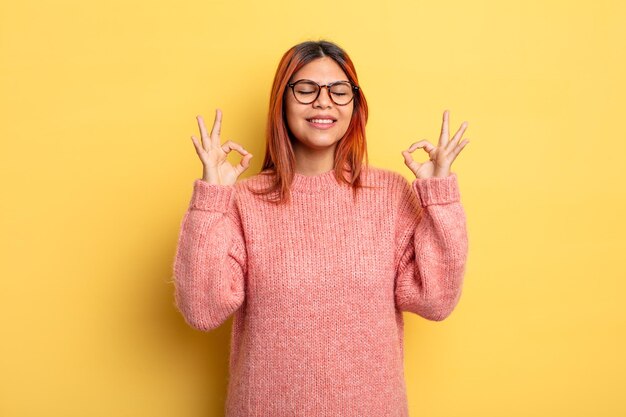 Jovem mulher hispânica olhando concentrada e meditando, sentindo-se satisfeita e relaxada, pensando ou fazendo uma escolha