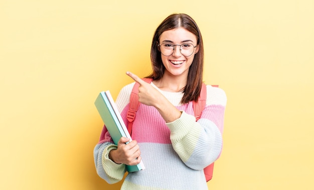 Jovem mulher hispânica parecendo animada e surpresa, apontando para o lado. conceito de estudante