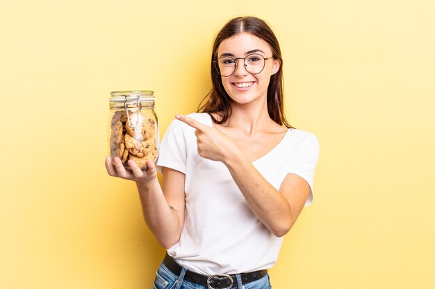 Jovem mulher hispânica parecendo animada e surpresa, apontando para o lado. conceito de garrafa de biscoitos