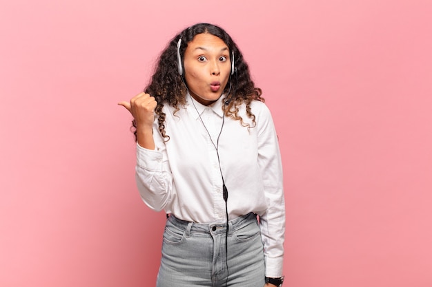 Jovem mulher hispânica parecendo espantada em descrença, apontando para o objeto ao lado e dizendo uau, inacreditável. conceito de telemarketing