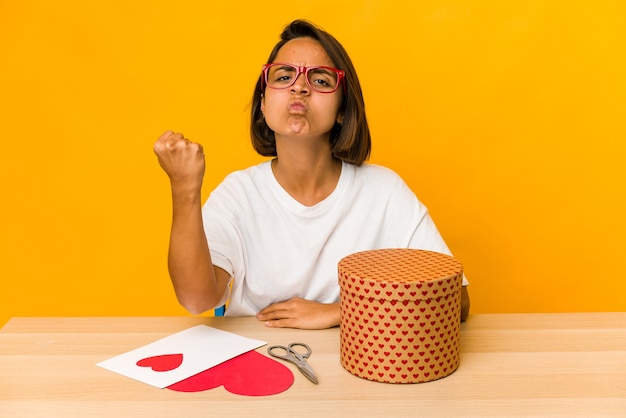 Jovem mulher hispânica preparando um presente de dia dos namorados isolado, mostrando o punho para a câmera, expressão facial agressiva.