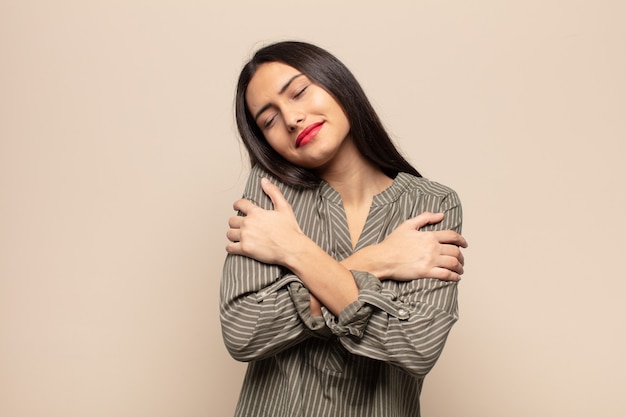 Jovem mulher hispânica se sentindo apaixonada, sorrindo, se acariciando e se abraçando, permanecendo solteira, sendo egoísta e egocêntrica