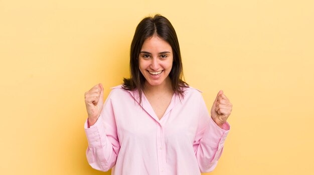 Jovem mulher hispânica se sentindo chocada, animada e feliz rindo e comemorando o sucesso dizendo uau