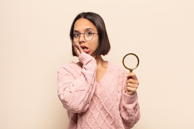 Foto jovem mulher hispânica se sentindo chocada e assustada, parecendo apavorada com a boca aberta e as mãos nas bochechas