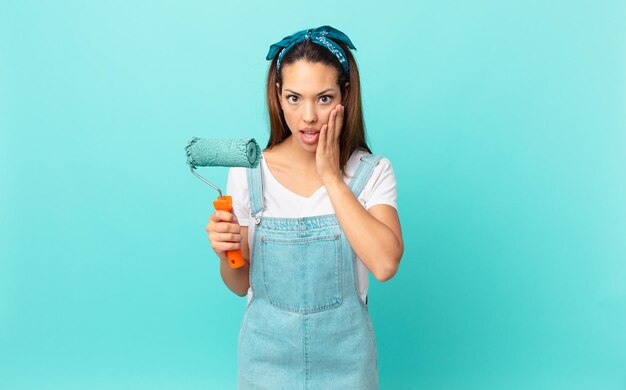 Jovem mulher hispânica se sentindo chocada e com medo e pintando uma parede