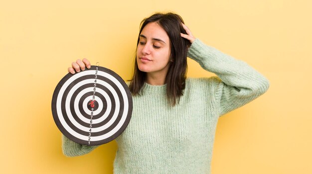 Jovem mulher hispânica se sentindo confusa e confusa coçando o conceito de alvo de dardos de cabeça