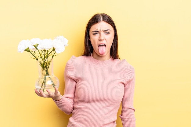 Jovem mulher hispânica se sentindo enojada e irritada e com a língua de fora. conceito de vaso de flores