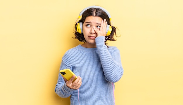 Jovem mulher hispânica se sentindo entediada, frustrada e com sono depois de um cansativo. conceito de fones de ouvido e smartphone