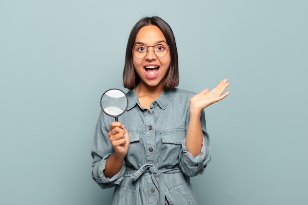 Jovem mulher hispânica se sentindo feliz, animada, surpresa ou chocada, sorrindo e espantada com algo inacreditável