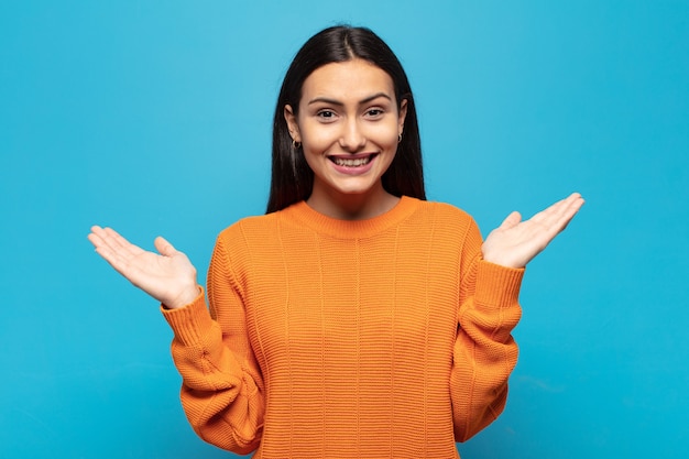 Jovem mulher hispânica se sentindo feliz, animada, surpresa ou chocada, sorrindo e espantada com algo inacreditável