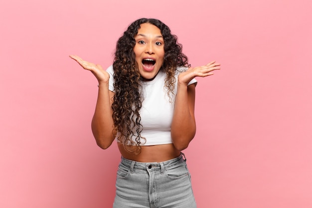 Jovem mulher hispânica se sentindo feliz, animada, surpresa ou chocada, sorrindo e espantada com algo inacreditável