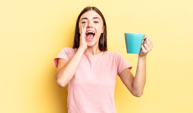 Jovem mulher hispânica se sentindo feliz, dando um grande grito com as mãos perto da boca. conceito de xícara de café
