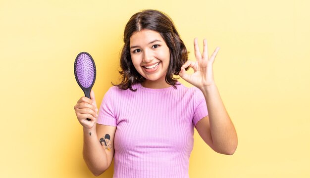 Jovem mulher hispânica se sentindo feliz, mostrando aprovação com gesto bem. conceito de escova de cabelo