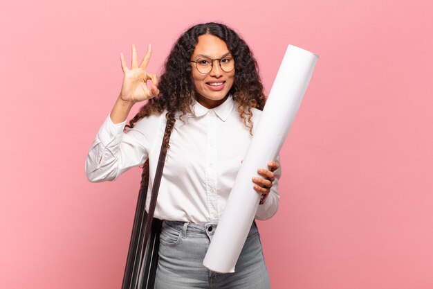 Jovem mulher hispânica se sentindo feliz, relaxada e satisfeita, mostrando aprovação com um gesto certo, sorrindo. conceito de arquiteto