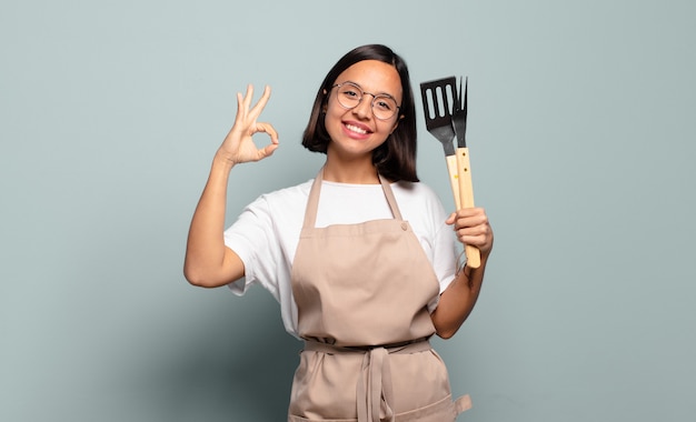 Jovem mulher hispânica se sentindo feliz, relaxada e satisfeita, mostrando aprovação com um gesto de ok, sorrindo