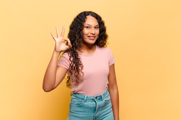 Foto jovem mulher hispânica se sentindo feliz, relaxada e satisfeita, mostrando aprovação com um gesto de ok, sorrindo