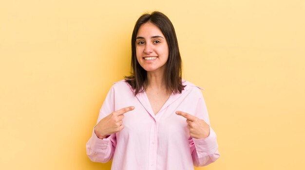 Jovem mulher hispânica se sentindo feliz, surpreso e orgulhoso, apontando para si mesmo com um olhar espantado e animado