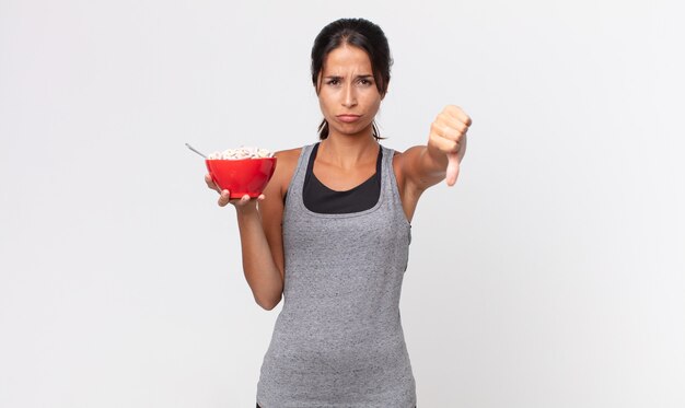 Jovem mulher hispânica se sentindo mal, mostrando os polegares para baixo. dieta de fitness e conceito de café da manhã