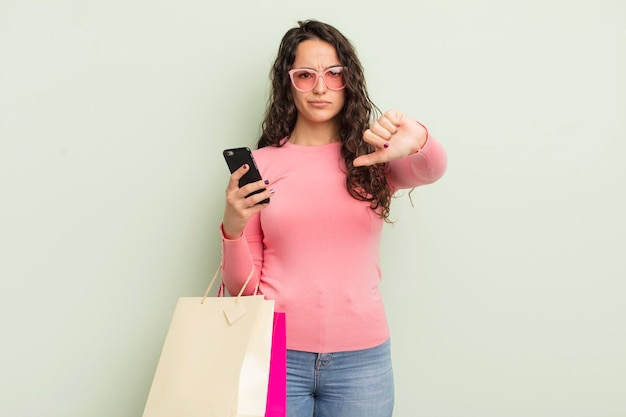 Jovem mulher hispânica se sentindo mostrando os polegares para baixo conceito de sacolas de compras