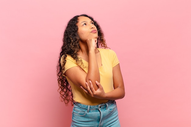 Jovem mulher hispânica se sentindo pensativa, imaginando ou imaginando ideias, sonhando acordada e olhando para cima para copiar o espaço