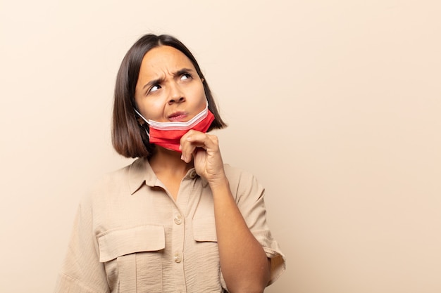 Jovem mulher hispânica se sentindo pensativa, imaginando ou imaginando ideias, sonhando acordada e olhando para copiar o espaço