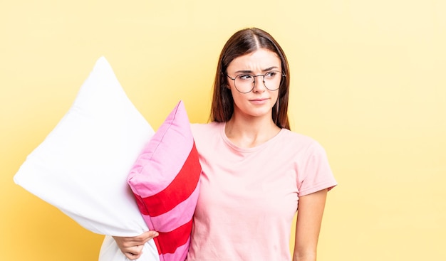 Jovem mulher hispânica se sentindo triste, chateada ou com raiva e olhando para o lado. conceito de pijama e travesseiro