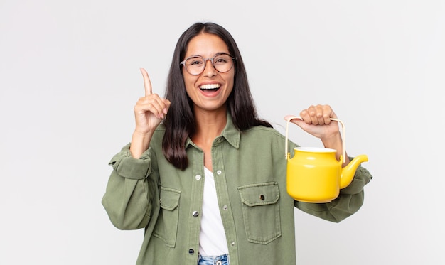 Jovem mulher hispânica se sentindo um gênio feliz e animado depois de perceber uma ideia e segurar um bule de chá