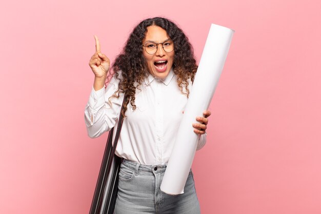 Jovem mulher hispânica se sentindo um gênio feliz e animado depois de realizar uma ideia, levantando o dedo alegremente, eureka !. conceito de arquiteto