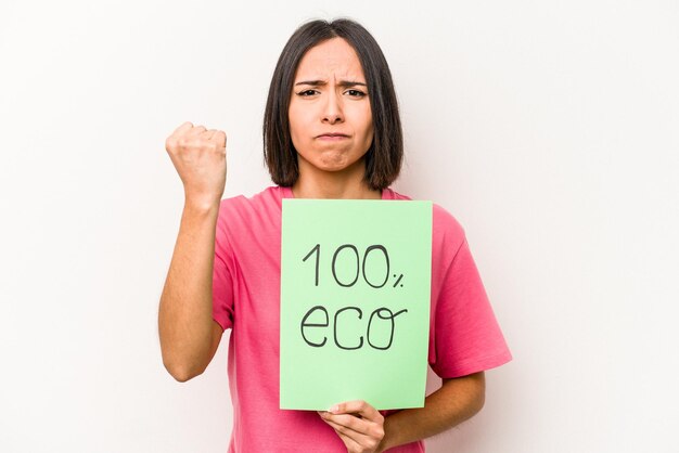 Jovem mulher hispânica segurando 100 eco cartaz isolado no fundo branco, mostrando o punho para a câmera expressão facial agressiva