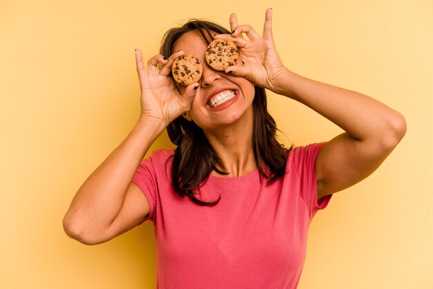 Jovem mulher hispânica segurando biscoitos isolados em fundo amarelo