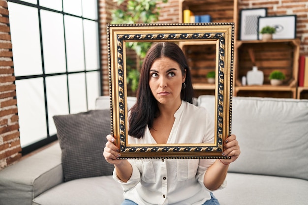 Foto jovem mulher hispânica segurando quadro vazio cético e nervoso franzeando a testa chateado por causa do problema pessoa negativa