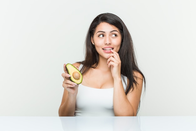 Jovem mulher hispânica, segurando um abacate relaxado pensando em algo