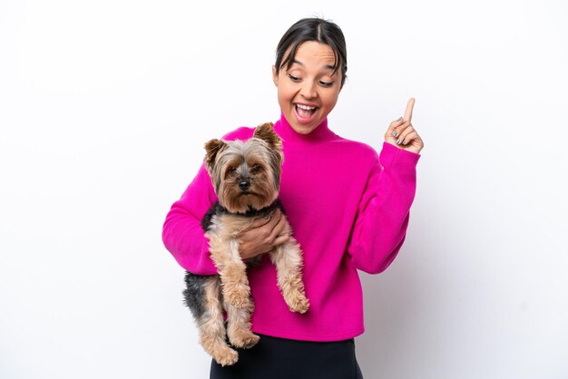 Foto jovem mulher hispânica segurando um cachorro isolado no fundo branco com a intenção de perceber a solução enquanto levanta um dedo