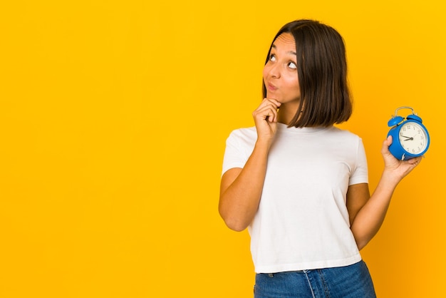 Jovem mulher hispânica segurando um megafone, olhando de soslaio com expressão duvidosa e cética.