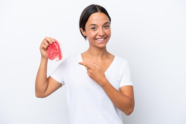 Jovem mulher hispânica segurando um pedaço de carne isolado no fundo branco e apontando-o