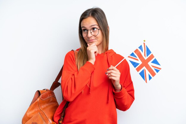 Jovem mulher hispânica segurando uma bandeira do Reino Unido isolada no fundo branco e olhando para cima